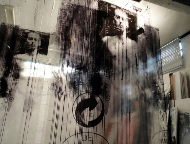 Black monochromatic prints on transparent material hung from the ceiling with a drippy appearance. These feature nude young men from the waist up. 