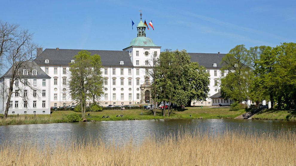 White baroque main building of Schloss Gottorf castle, with trees and body of water in front
