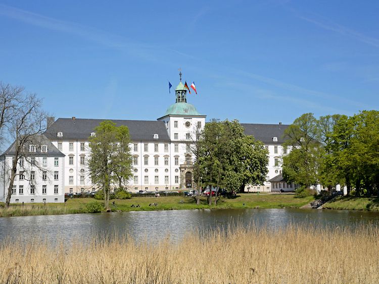  White baroque main building of Schloss Gottorf castle, with trees and body of water in front