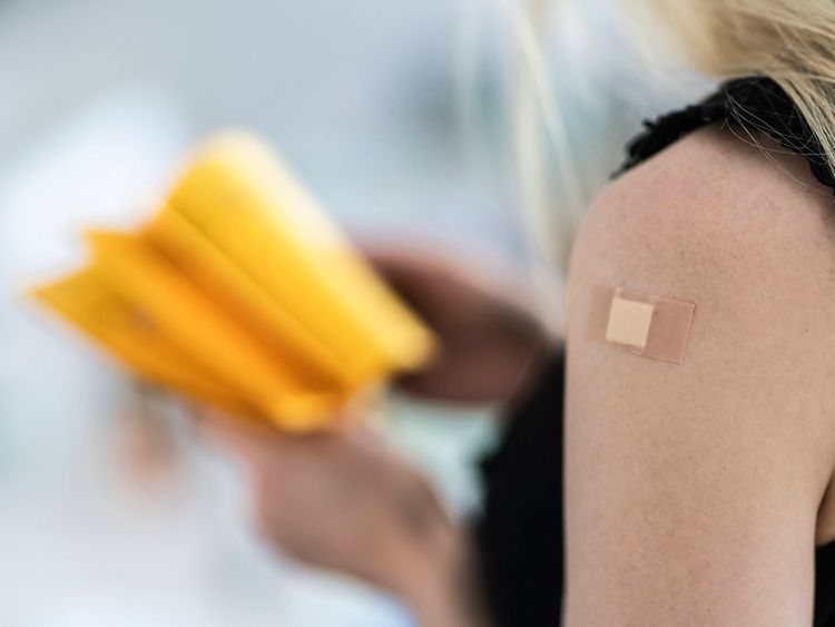  Close-up of a femals person's shoulder with a band aid; the person is holding a yellow vaccination pass.