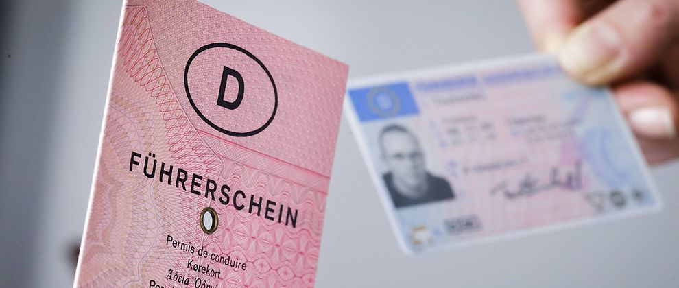  An old German driver's Licence with the title Führerschein translated into different languages. Next to it, in the background, a hand is holding a new EU driver's licence card.