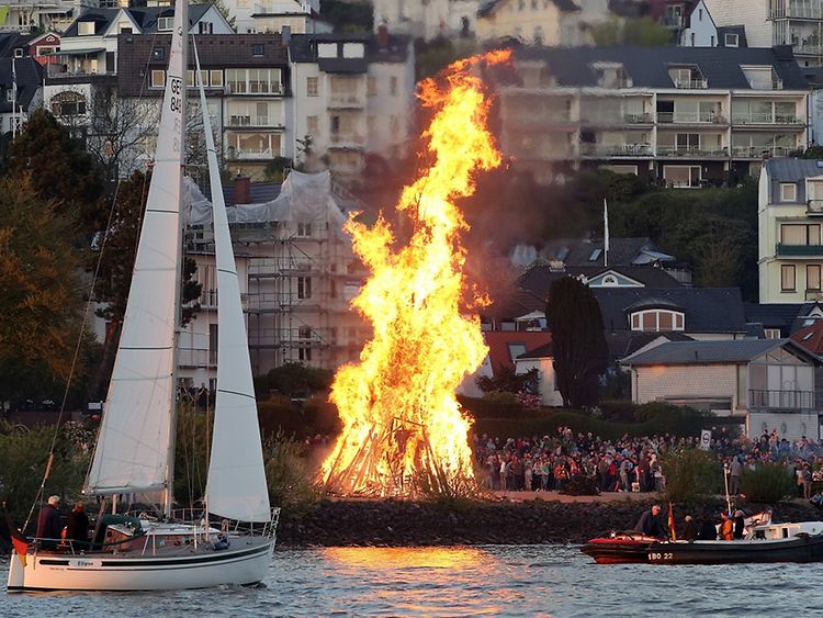  An Easter bonfire close to the Elbe river in Hamburg-Blankenese, with crowd gathering and sail boat and bark in front