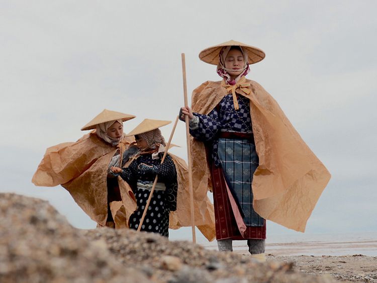  Drei Menschen in traditionell japanischer Kleidung an einem Steinstrand.