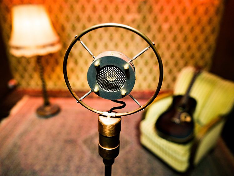  Vintage microphone on a stand on a stage with vintage lamp and acoustic guitar on vintage armchair in background
