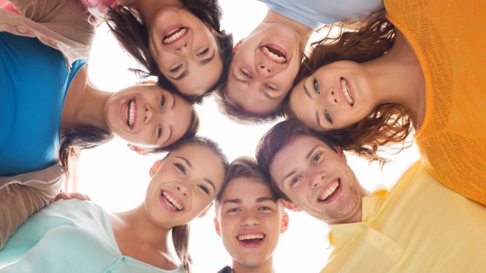 Seven young persons arranged in a circle smiling into the camera