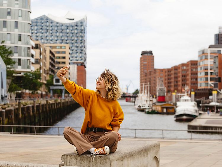  Woman taking picture of herself with HafenCity buildings and Elbphilharmonie in background