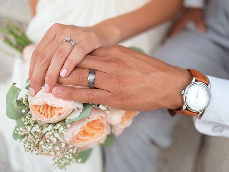  Two people touching hands upon a bouquet of flowers, wearing silver rings.